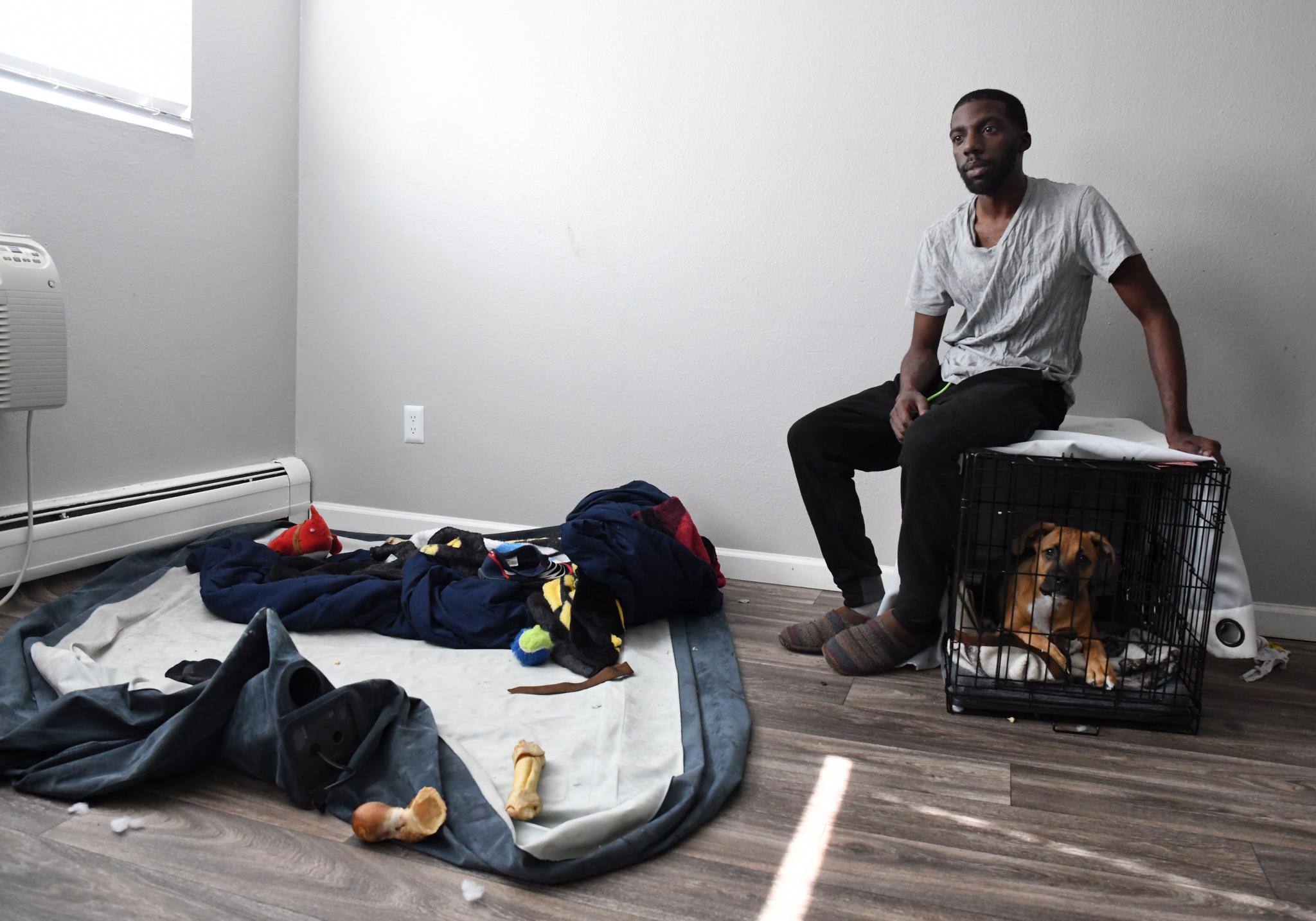 A man sits on top of a dog crate with the dog inside, next to an air mattress