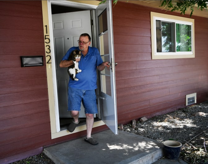A man steps outside of his home holding a cat
